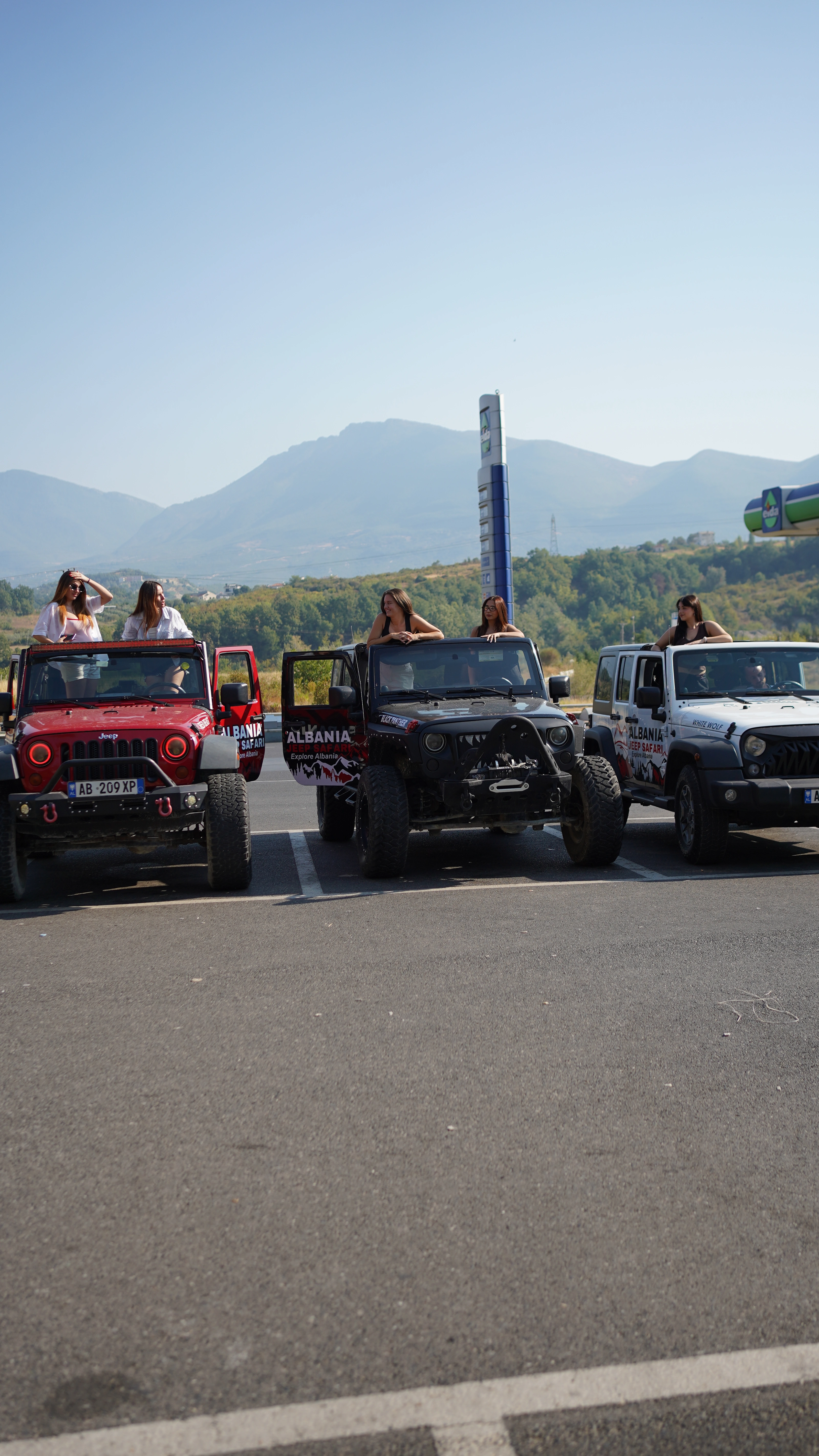 Three Jeep Wranglers lined up on the road, guests waving from the open tops, mountains behind