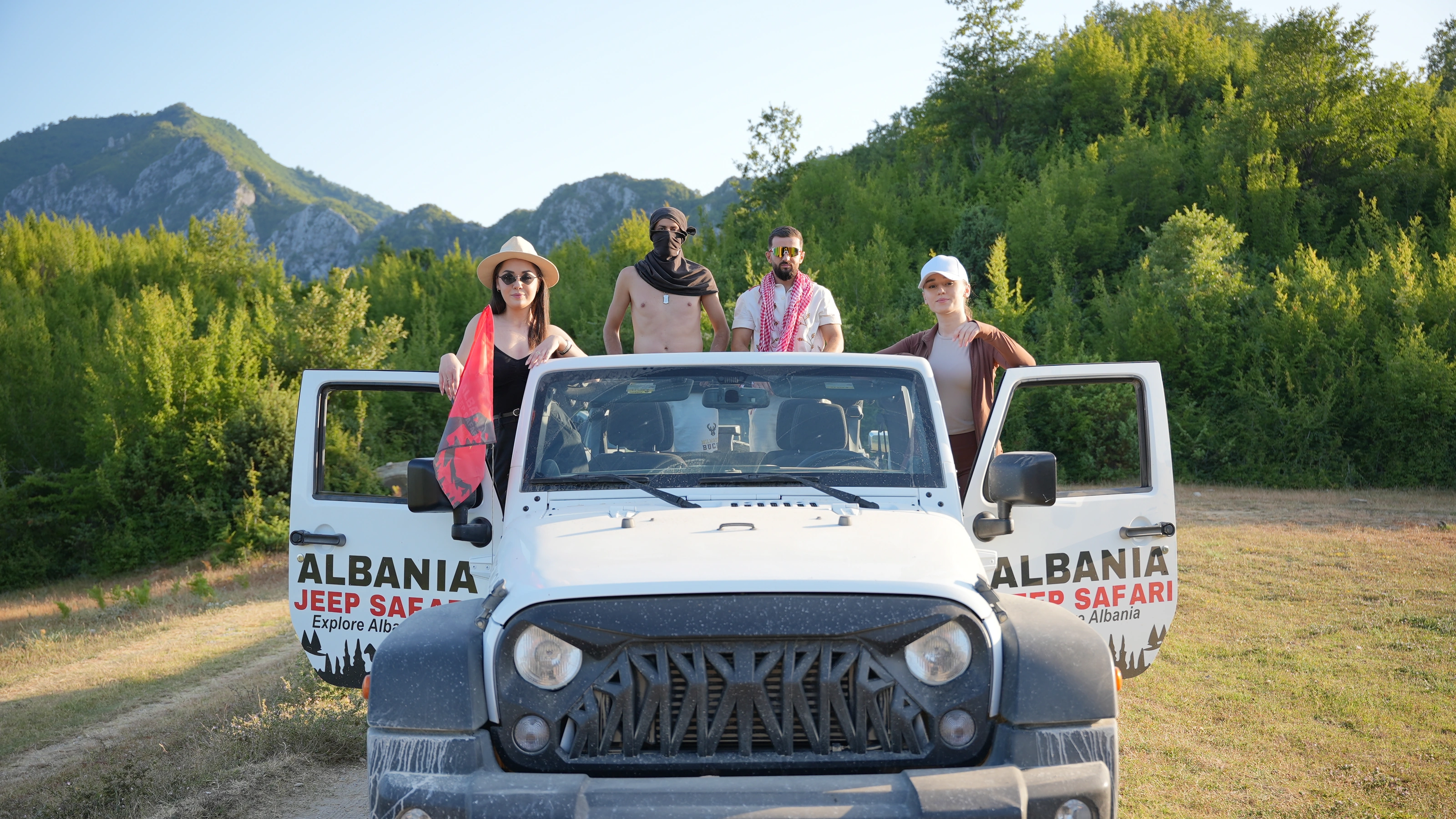 Guests posing on the white Wrangler, doors open, green hills behind